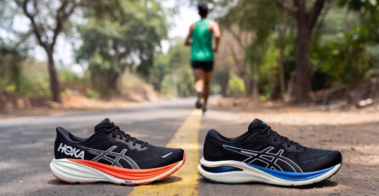 Hoka Clifton 10 and Asics Gel-Nimbus 27 max-cushion running shoes placed on an Indian dirt road, with a runner jogging in the background wearing green tank top during hot weather marathon training in Greater Noida 2026