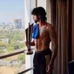 Tilak Varma posing shirtless with the T20 World Cup 2026 trophy by the window, showcasing his chiseled physique and fitness results the day after India's victory