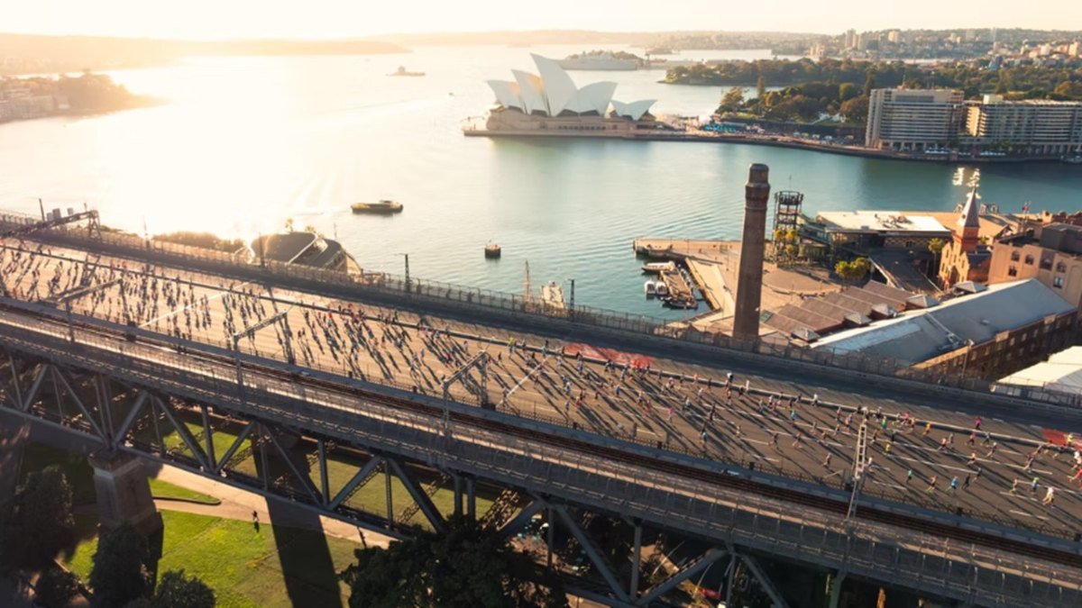 Runners crossing the Sydney Harbour Bridge at sunrise during the 2025 TCS Sydney Marathon, with the Opera House in the background