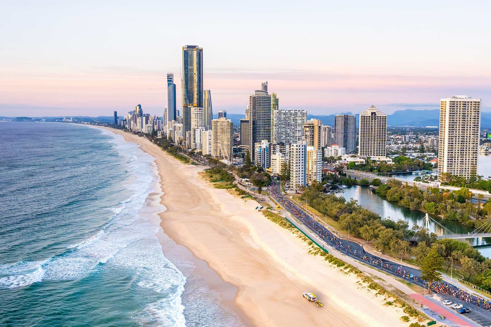 ASICS Gold Coast Marathon 2026 aerial view — thousands of runners race along the Gold Coast beachfront past Surfers Paradise skyline at sunrise