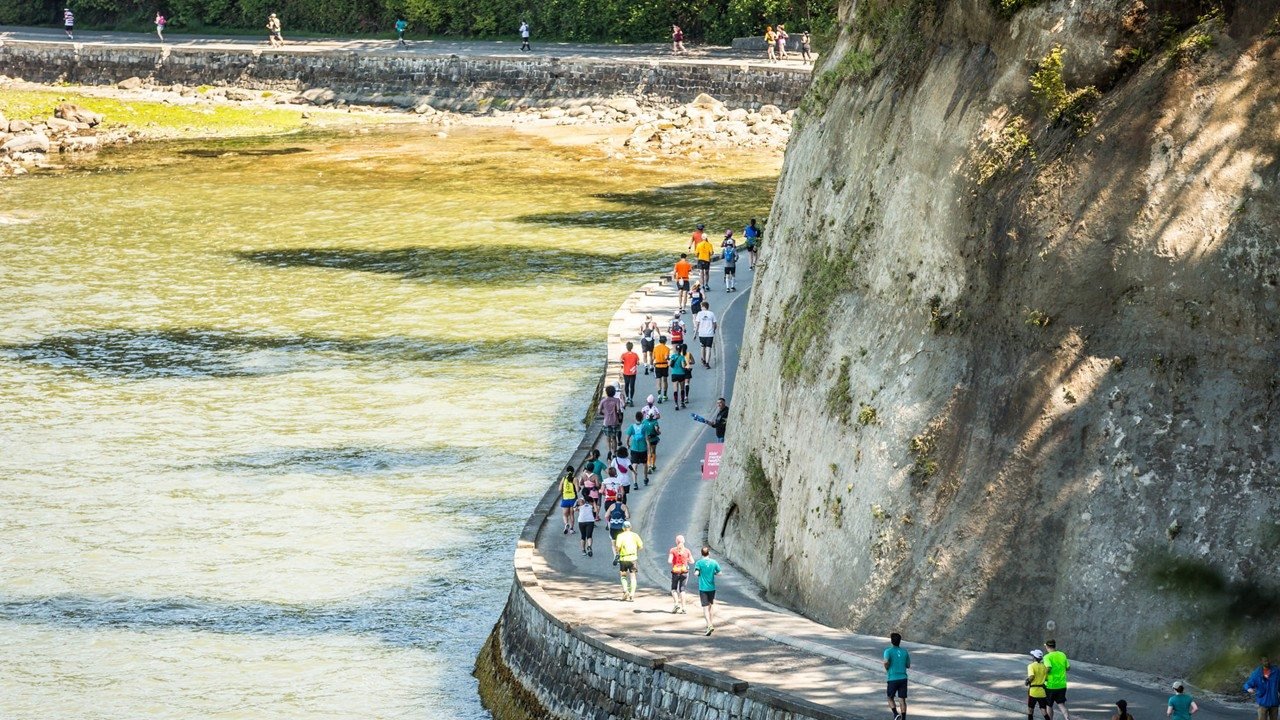 BMO Vancouver Marathon 2027: Complete Guide for International Runners 2 Runners at the BMO Vancouver Marathon passing along the iconic Stanley Park Seawall with mountains in the background