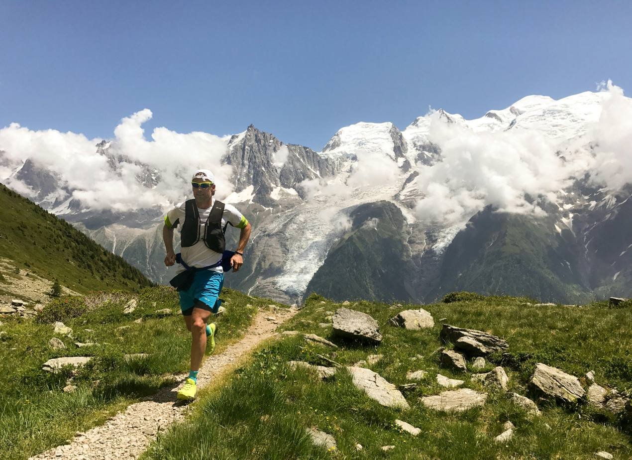 Trail runner on a rocky mountain path with snow-capped Alps in the background, ideal terrain for the Merrell MTL SpeedARC Peak