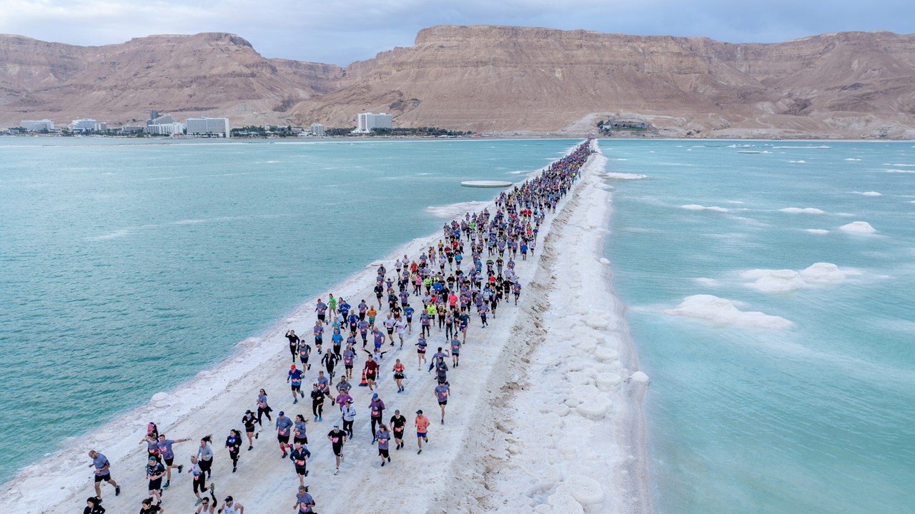 Dead Sea Marathon 2027: The Complete Race Guide to the Lowest Race on Earth 2 Runners on the Dead Sea Marathon course crossing the gravel dike with the Dead Sea and Moab Mountains in the background