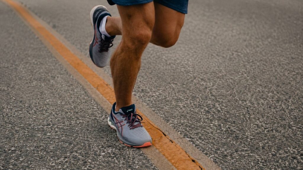 Runner in ASICS shoes training on road for marathon - mid-stride close-up showing running form