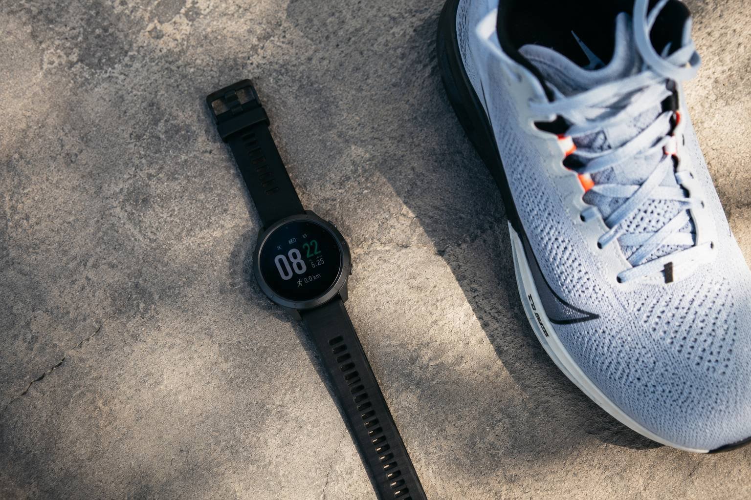 August 2026 Running Roundup: Brooks Hyperion Elite 6, Garmin Fenix 9 and Race News 1 Top-down view of a black GPS running watch and a performance running shoe on a concrete surface for the monthly running news and gear dispatch.