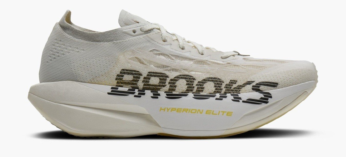 Brooks Hyperion Elite 6 lateral view showing flat-knit TPU upper, tan DNA Gold PEBA midsole stack and black Brooks wordmark on a near all-white colorway
