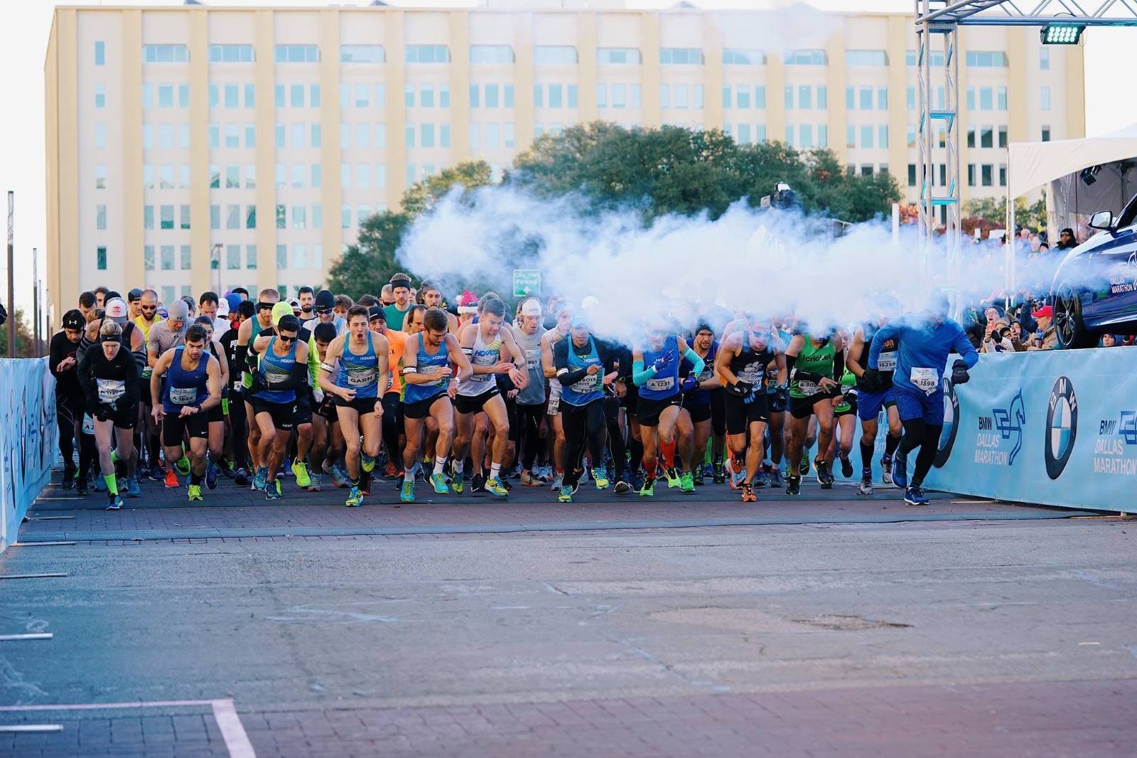 Runners surging off the starting line at the BMW Dallas Marathon in downtown Dallas, with race-day atmosphere at Dallas City Hall Plaza