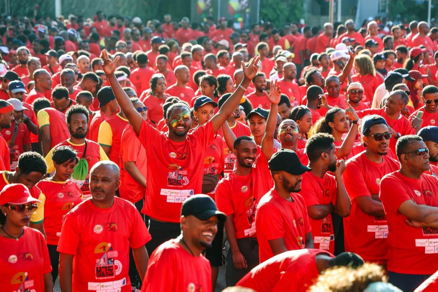 A dense crowd of runners in red race shirts at the Great Ethiopian Run in Addis Ababa, with one runner raising their arm at the mass start.