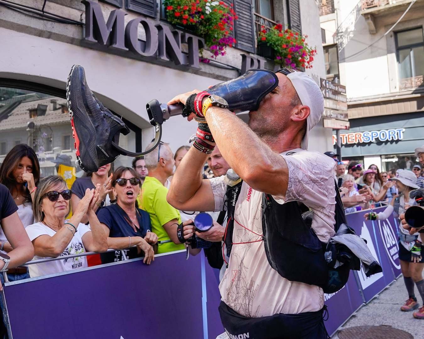 Julien Veysseyre drinks from his prosthetic running blade to celebrate finishing the UTMB in Chamonix while a crowd applauds.