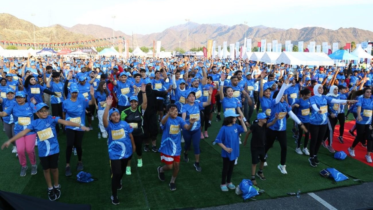 Thousands of runners in blue race t-shirts gathered at the start of the NBF Fujairah Run with the Hajar Mountains rising in the background