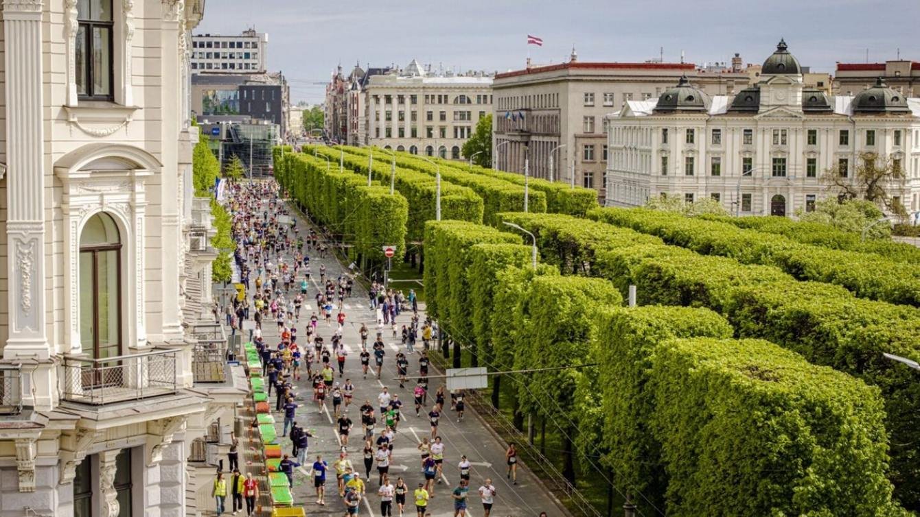 Runners racing along the tree-lined 11 November Embankment at the Rimi Riga Marathon with Riga's historic skyline in the background