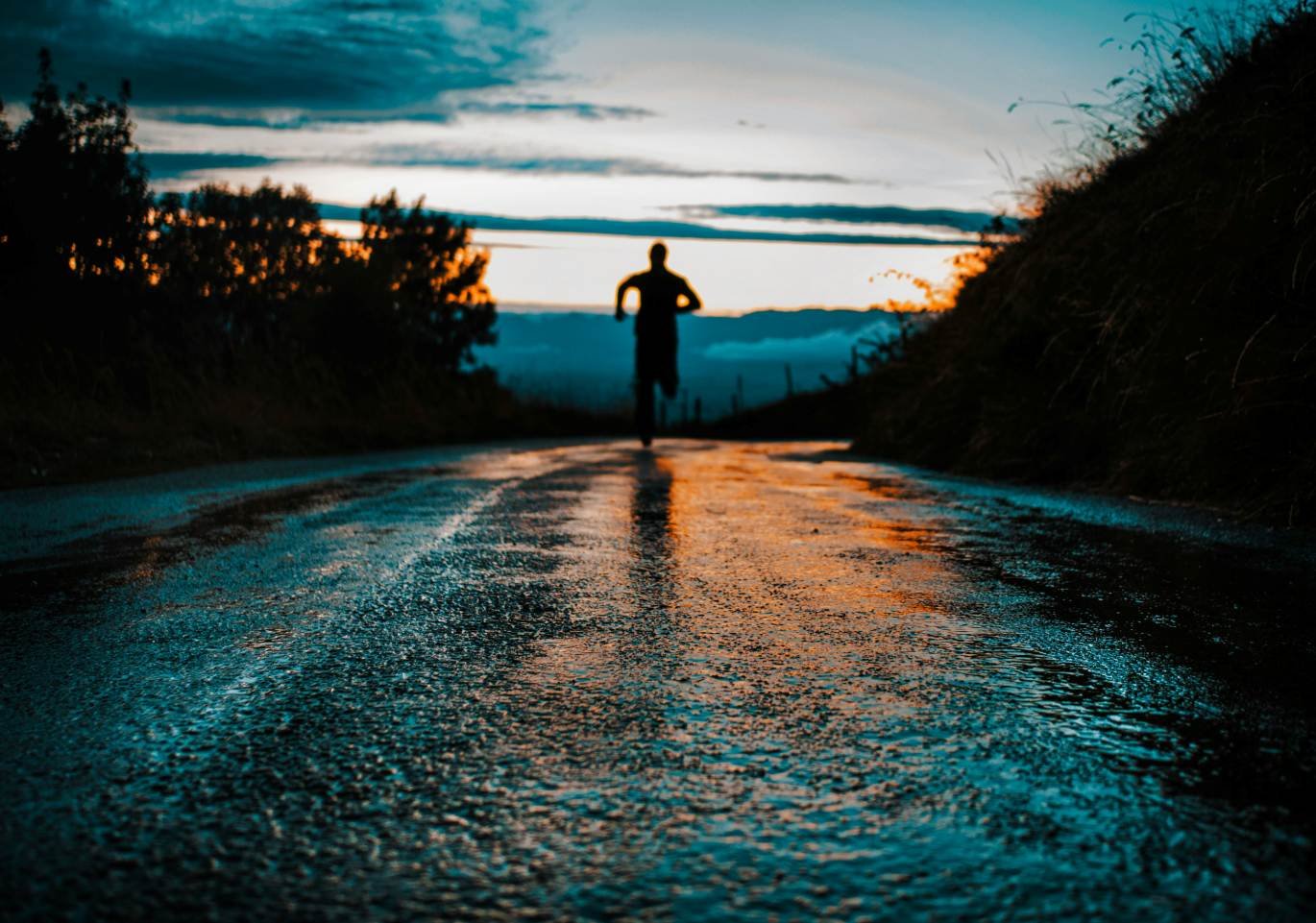 Silhouette of a runner on a wet road at dusk during monsoon rain.