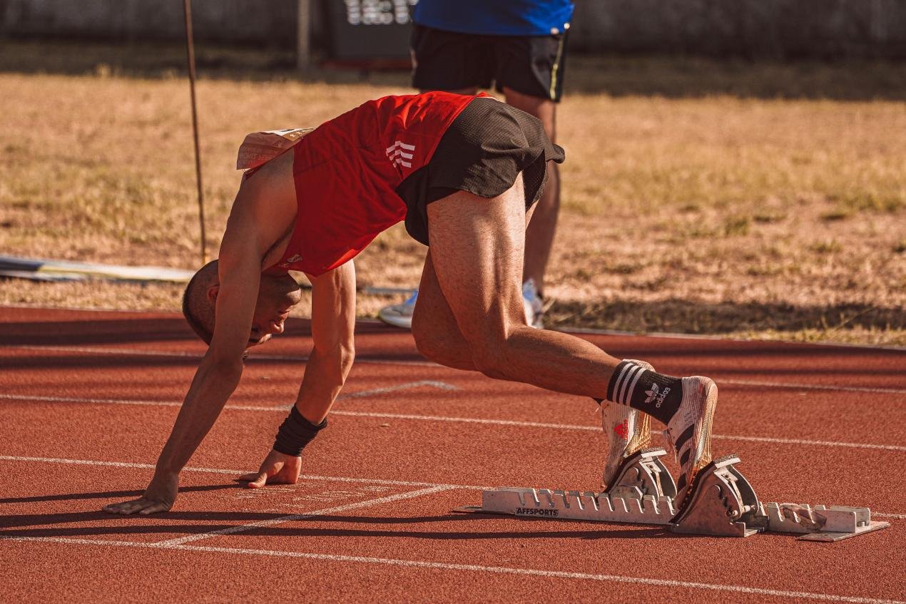 Speed Reserve Principle: How Short Hill Sprints Unlock Long-Distance Speed 1 Track sprinter set in starting blocks preparing to explode down the track, illustrating max velocity sprint mechanics and speed reserve training for distance runners.
