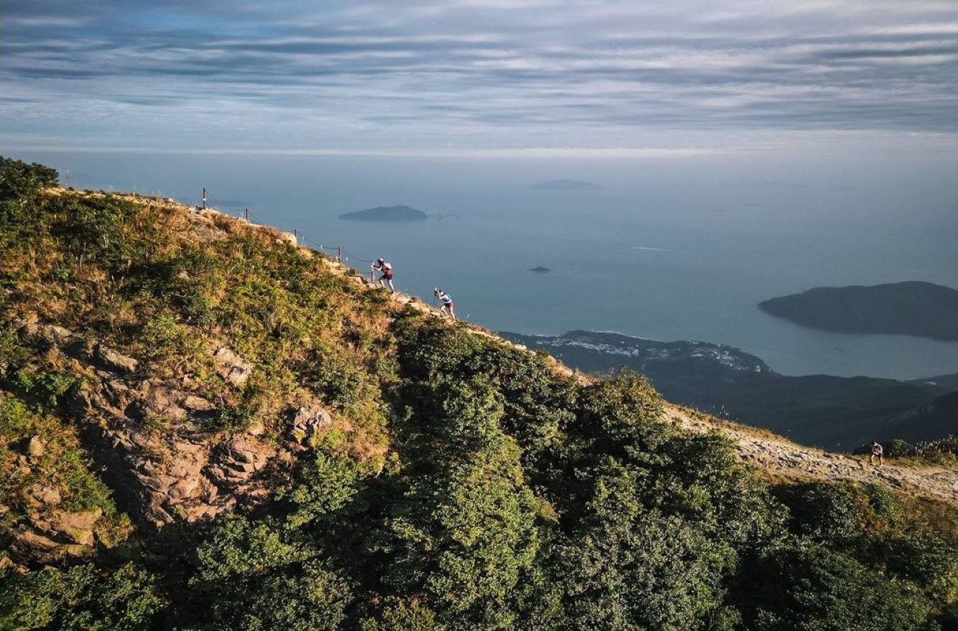 TransLantau by UTMB 2026 Race Guide: Courses, Registration and Tips 2 Runners on the singletrack trails of Lantau Island at TransLantau by UTMB 2026, with hills and coastal scenery in the background