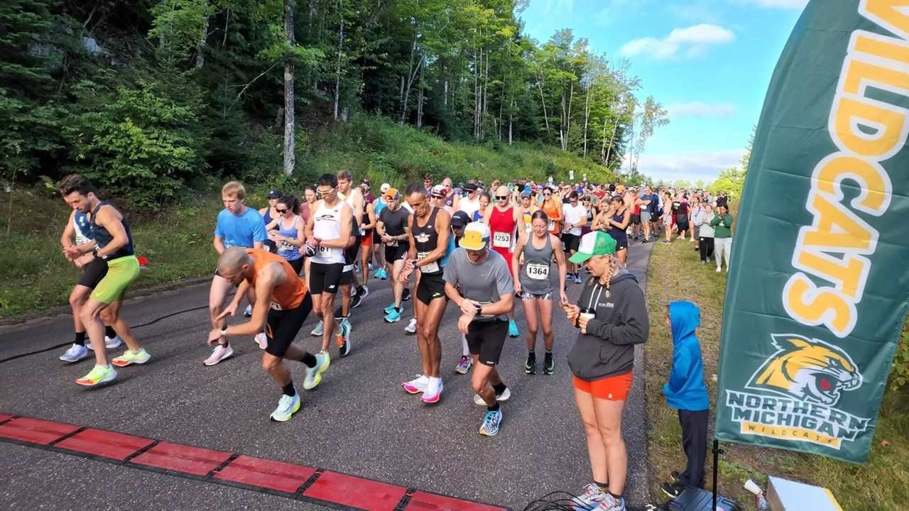 2027 Marquette Marathon Registration Is Now Open 1 Runners at the start of the Marquette Marathon in Ishpeming, Michigan, with the Northern Michigan University Wildcats banner visible at the start line