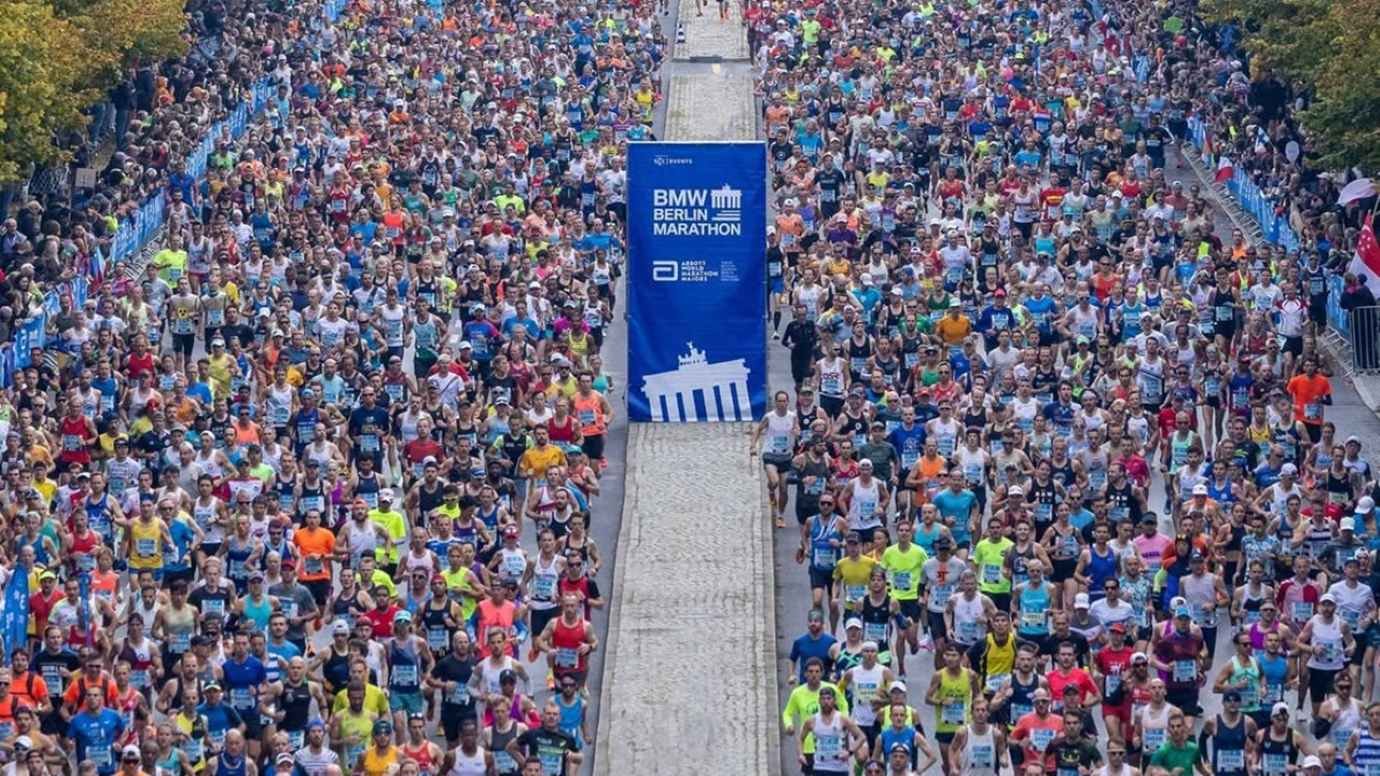 60,000 runners packed on Straße des 17. Juni at the BMW Berlin Marathon 2026 start, with the Brandenburg Gate visible through the autumn trees.