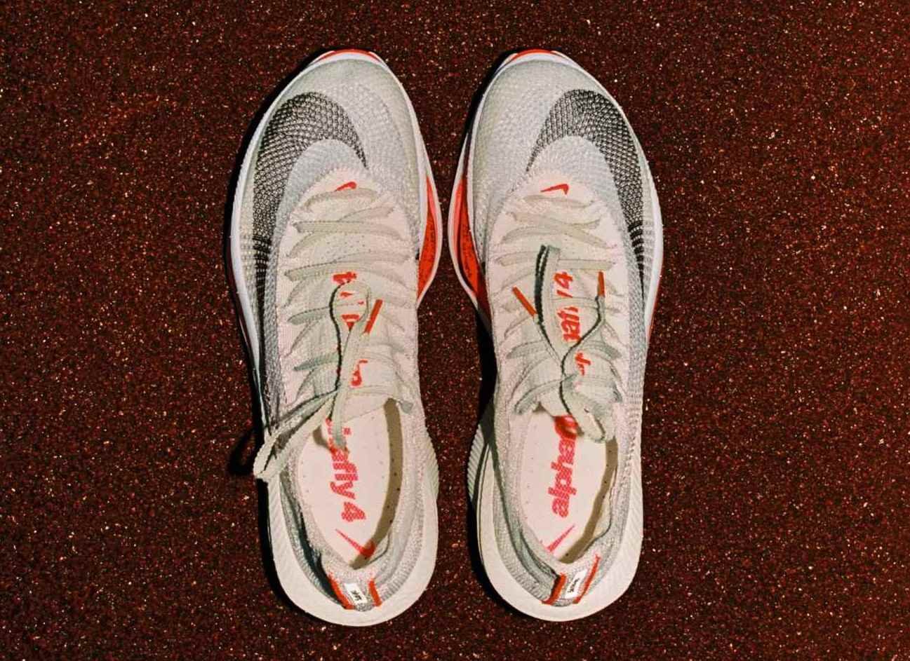 Nike Alphafly 4 marathon racing shoes seen from above, showing the new Atomknit upper in off-white with red accents, on a red track surface
