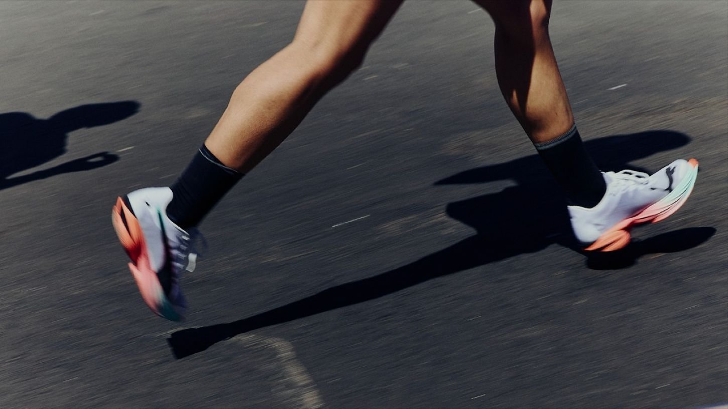 A runner mid-stride on asphalt wearing PUMA Fast-R NITRO Elite racing shoes with orange accents — part of the PUMA Project3 programme kit