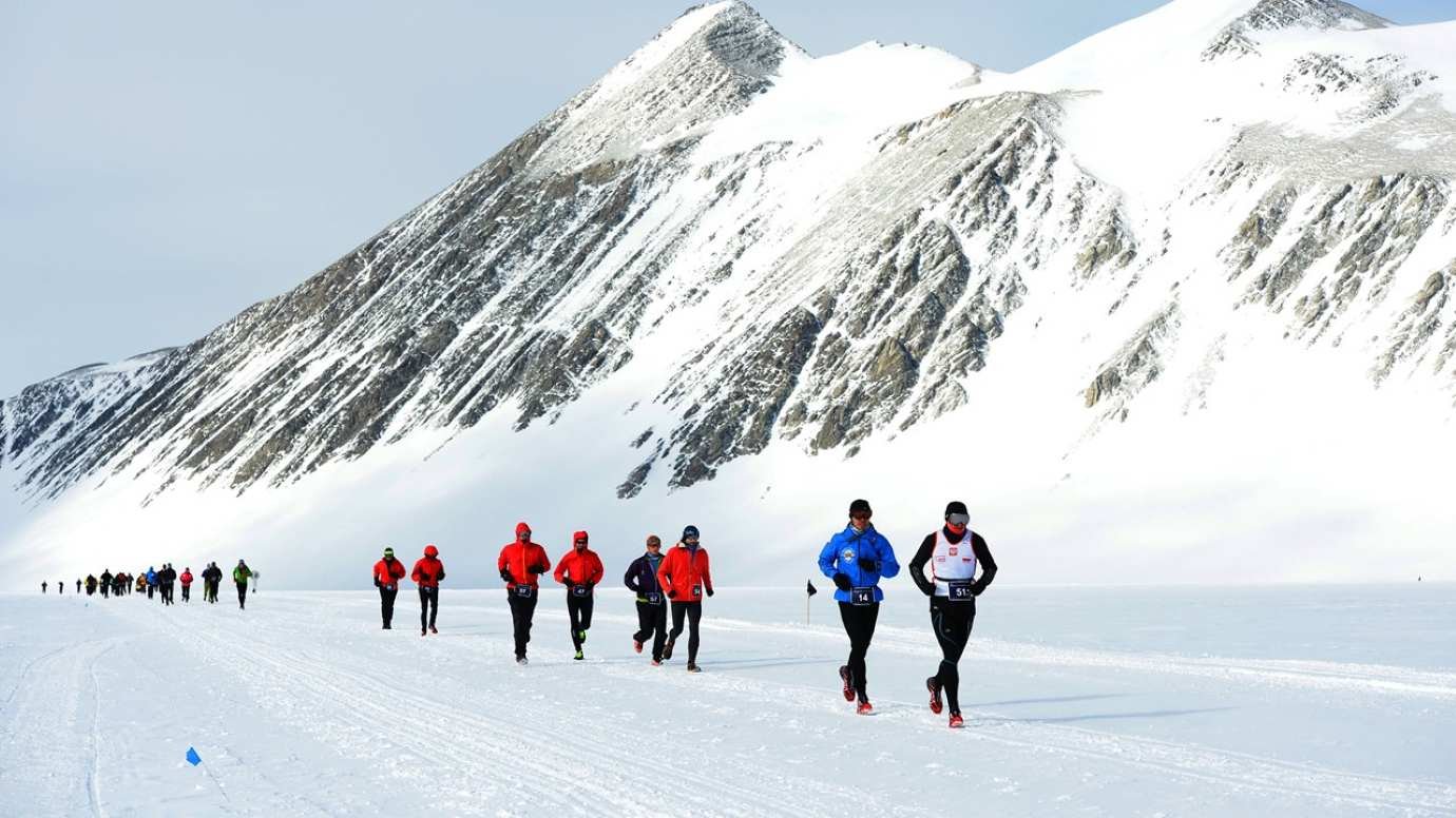 Runners race across the Union Glacier ice sheet at the Antarctic Ice Marathon, with snow-covered peaks rising behind them