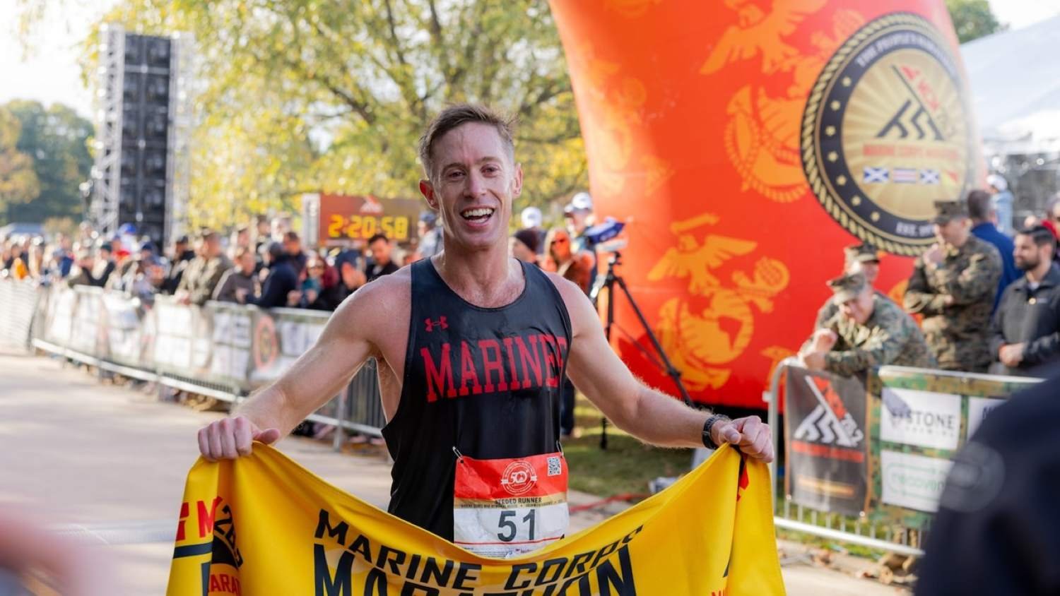 Kyle King crosses the Marine Corps Marathon finish line in a Marines vest holding the MCM finisher banner