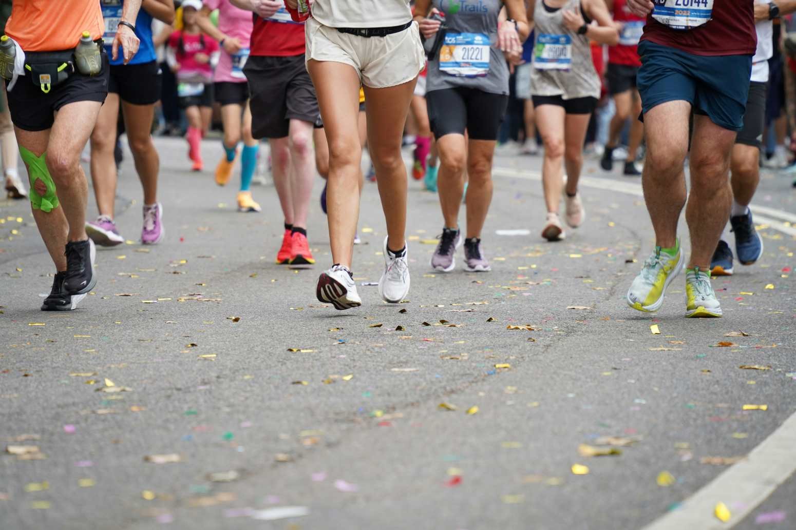 Marathon runners in the TCS New York City Marathon passing through Central Park, with confetti scattered on the road