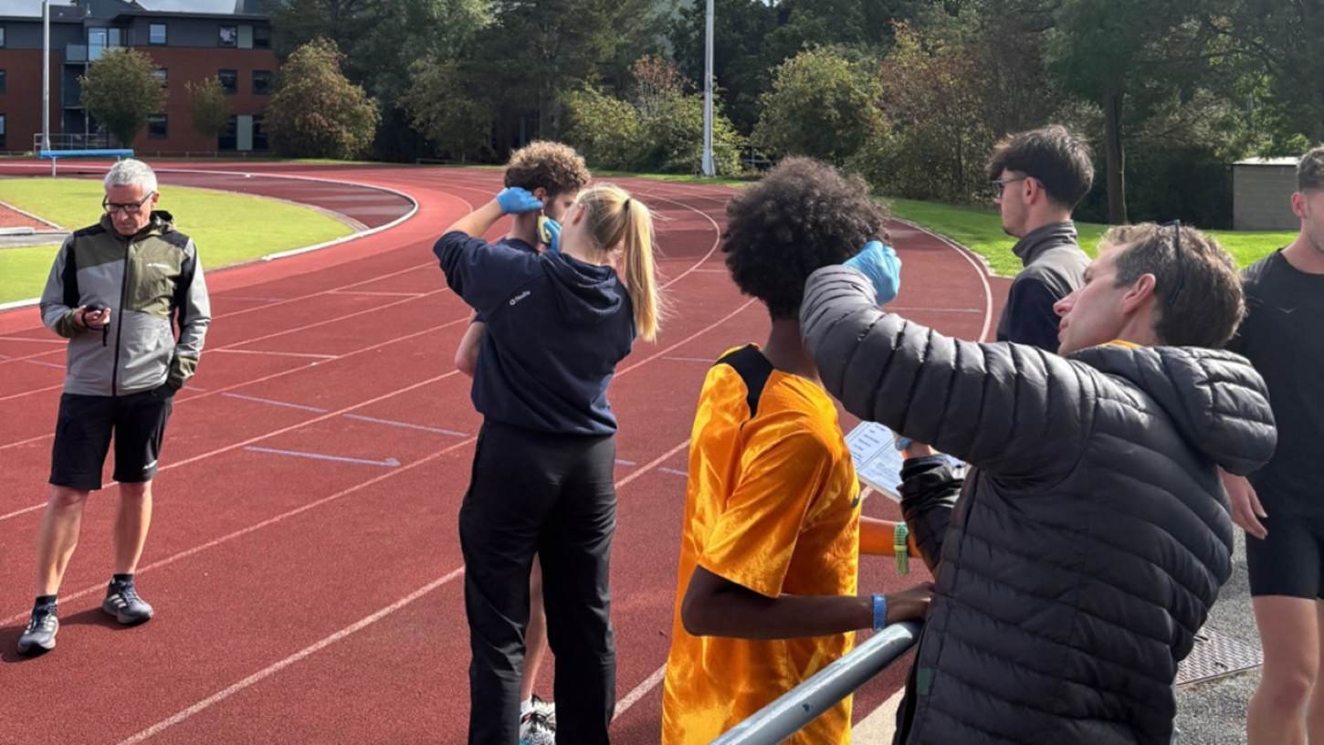 Practitioners in blue gloves conduct trackside physiology testing on athletes during the inaugural Project Brisbane camp at Leeds Beckett University's Carnegie School of Sport