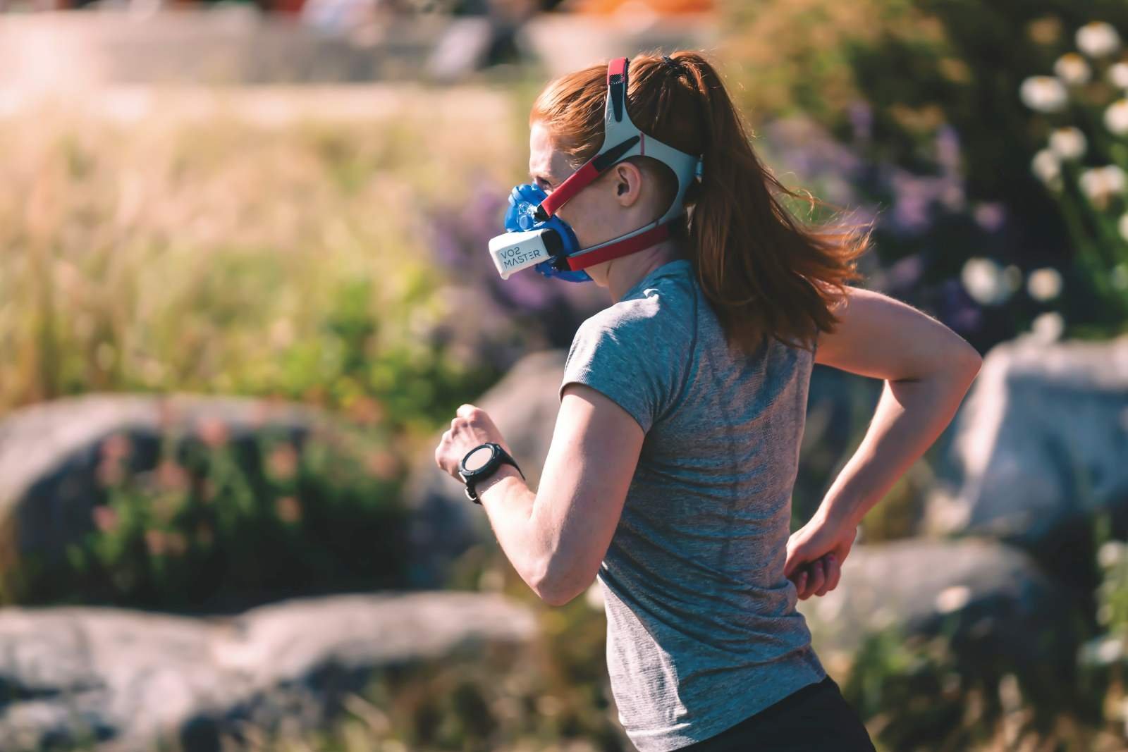Female runner wearing a VO2 Master oxygen measurement mask during an outdoor run, with a GPS watch on her wrist