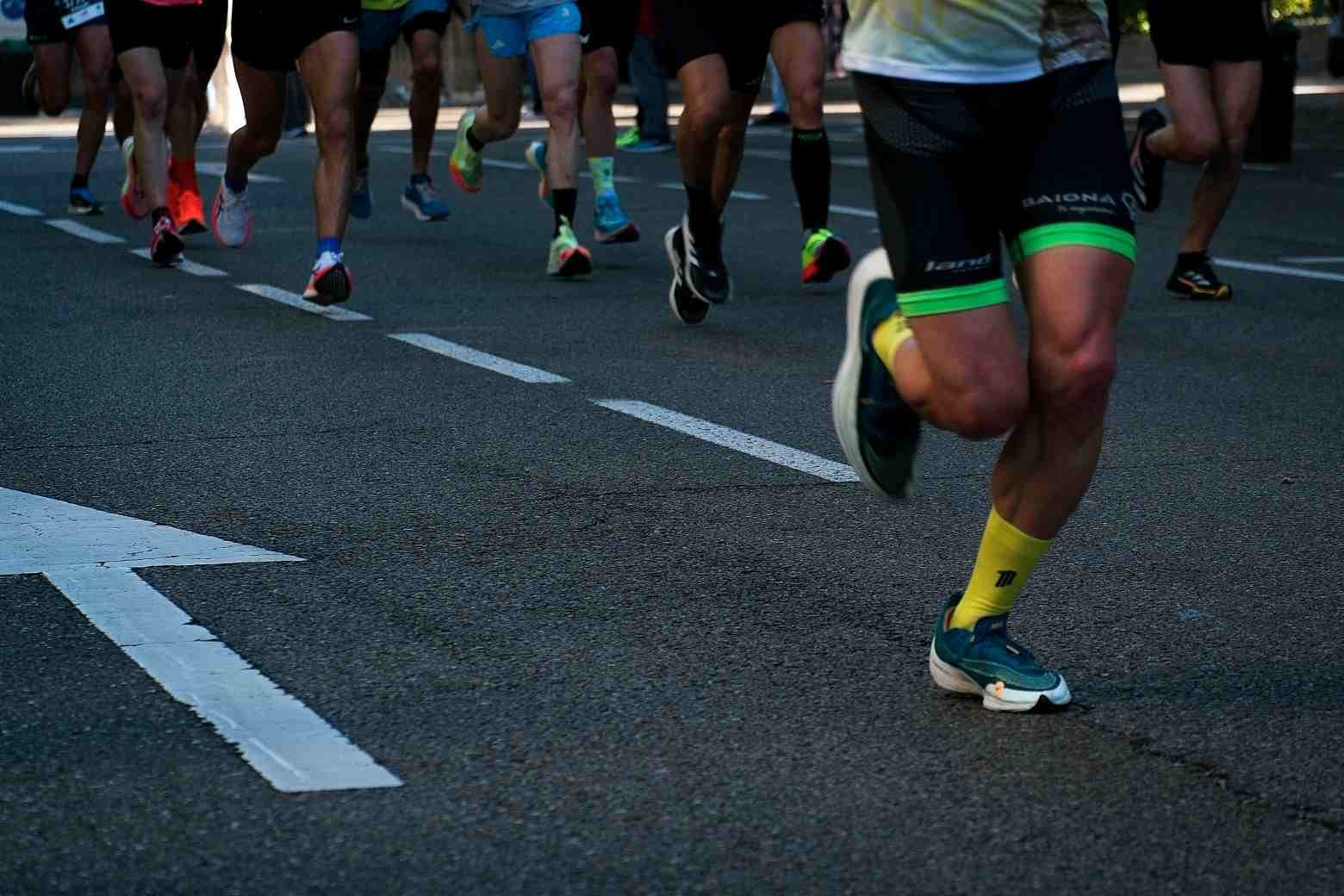 Runners' legs mid-stride during a road race, showing knee drive and foot strike mechanics
