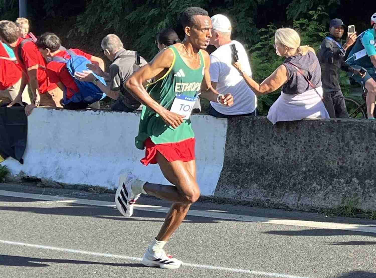 Tamirat Tola of Ethiopia competing in the men's marathon at the Paris 2024 Olympics, wearing the green Ethiopia vest and red shorts